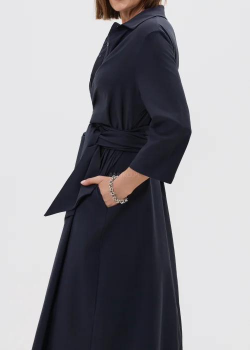 Granatowa sukienka midi o kopertowym kroju z wiązaniem w talii i rękawem 3/4, zestawiona z wysokimi czarnymi kozakami w eleganckiej stylizacji.