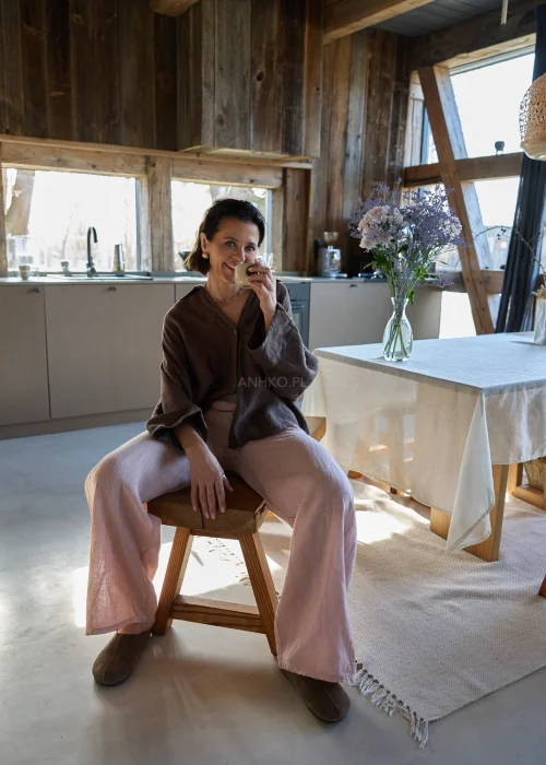 Brązowa lniana koszula oversize z długim rękawem i guzikami, o luźnym fasonie, zestawiona z jasnymi spodniami, stylizacja w naturalnym, minimalistycznym klimacie.
