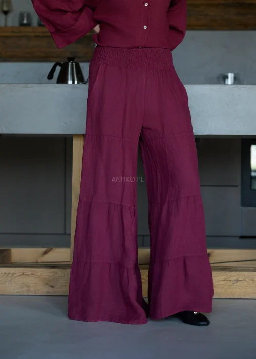 Szerokie spodnie damskie z wysokim stanem w kolorze bordowym, o luźnym kroju z marszczoną talią i rozszerzanymi nogawkami, stylizacja w minimalistycznym, eleganckim klimacie.
