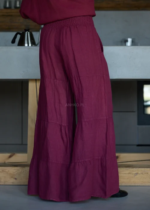 Szerokie spodnie damskie z wysokim stanem w kolorze bordowym, o luźnym kroju z marszczoną talią i rozszerzanymi nogawkami, stylizacja w minimalistycznym, eleganckim klimacie.