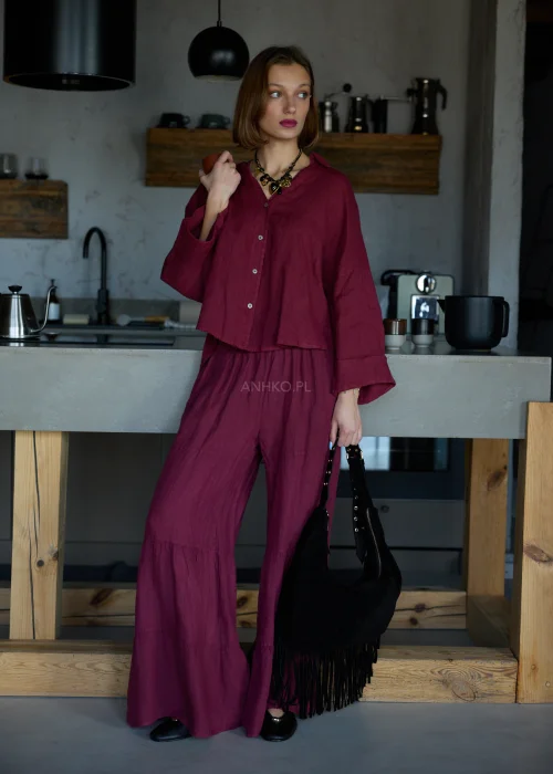 Szerokie spodnie damskie z wysokim stanem w kolorze bordowym, o luźnym kroju z marszczoną talią i rozszerzanymi nogawkami, stylizacja w minimalistycznym, eleganckim klimacie.