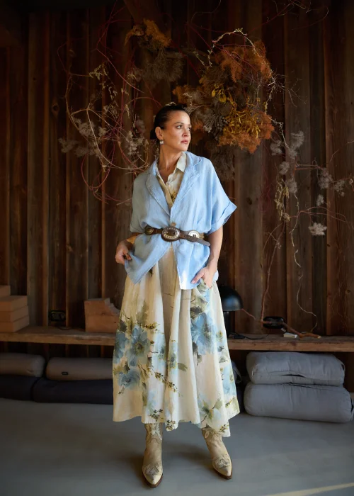 Lniana sukienka koszulowa maxi w beżowym kolorze z delikatnym kwiatowym wzorem, o luźnym kroju z krótkim rękawem i zapięciem na guziki, stylizacja w naturalnym, eleganckim klimacie.