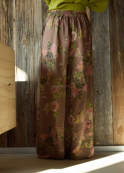 Szerokie spodnie damskie z wysokim stanem w brązowym kolorze z kwiatowym wzorem, o luźnym, lejącym kroju z elastyczną talią, stylizacja w naturalnym, boho klimacie.
