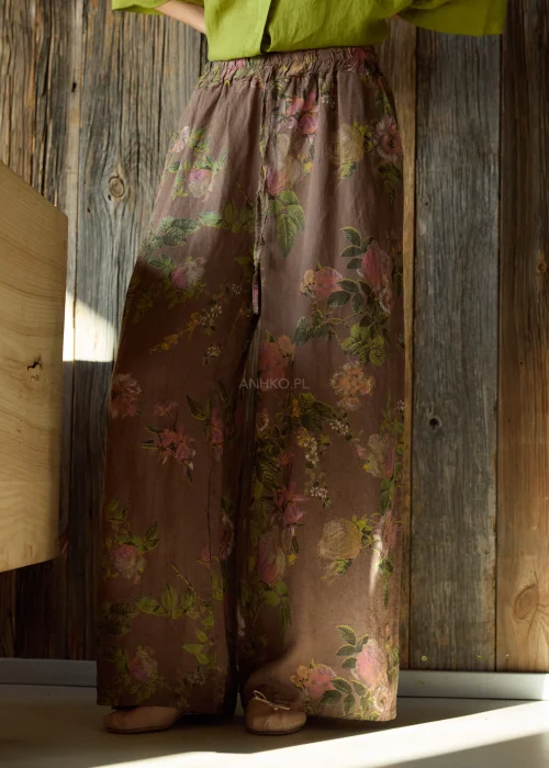 Szerokie spodnie damskie z wysokim stanem w brązowym kolorze z kwiatowym wzorem, o luźnym, lejącym kroju z elastyczną talią, stylizacja w naturalnym, boho klimacie.
