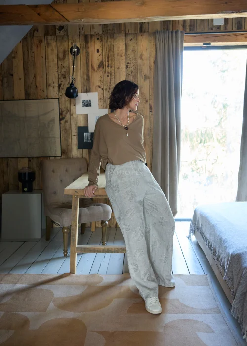 Lniane spodnie w szarym kolorze z subtelnym roślinnym wzorem, o szerokiej nogawce i luźnym kroju, stylizowane z paskiem w naturalnym odcieniu w minimalistycznym, eleganckim looku.