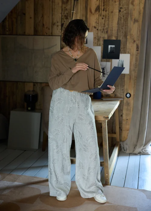 Lniane spodnie w szarym kolorze z subtelnym roślinnym wzorem, o szerokiej nogawce i luźnym kroju, stylizowane z paskiem w naturalnym odcieniu w minimalistycznym, eleganckim looku.