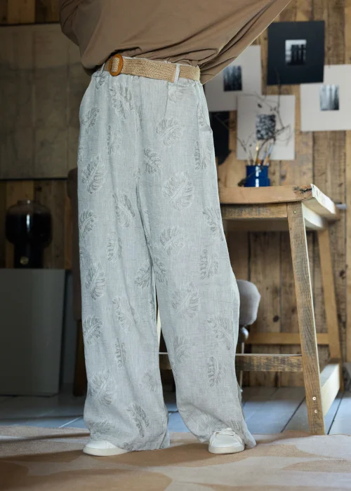 Lniane spodnie w szarym kolorze z subtelnym roślinnym wzorem, o szerokiej nogawce i luźnym kroju, stylizowane z paskiem w naturalnym odcieniu w minimalistycznym, eleganckim looku.