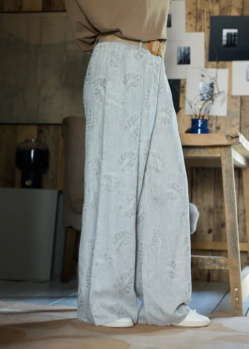 Lniane spodnie w szarym kolorze z subtelnym roślinnym wzorem, o szerokiej nogawce i luźnym kroju, stylizowane z paskiem w naturalnym odcieniu w minimalistycznym, eleganckim looku.