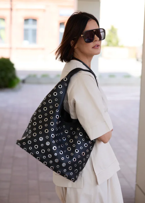 Czarna torba damska z kosmetyczką i ozdobnymi metalowymi oczkami w nowoczesnym stylu urban chic. Miękki model shopper z efektownymi detalami, idealny do codziennych stylizacji.