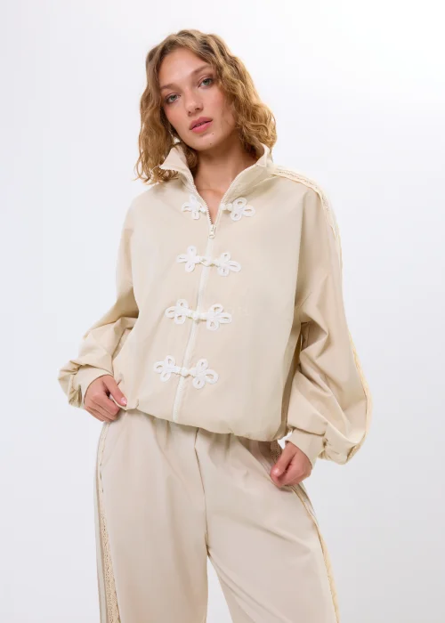 Beżowa bluza oversize na zamek z ozdobnymi wiązaniami i wysokim kołnierzem. Luźny fason nadaje stylizacji nowoczesny i oryginalny charakter.