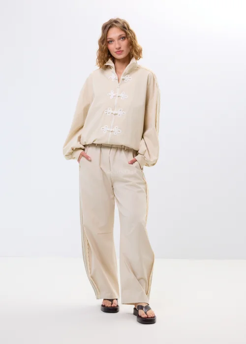 Beżowa bluza oversize na zamek z ozdobnymi wiązaniami i wysokim kołnierzem. Luźny fason nadaje stylizacji nowoczesny i oryginalny charakter.