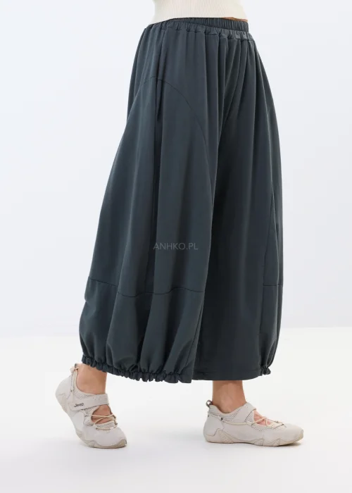 Grafitowe spodnie dresowe o szerokim, balonowym fasonie z elastycznym wykończeniem nogawek. Casualowe spodnie oversize w nowoczesnym stylu zestawione ze sportowymi sneakersami.
