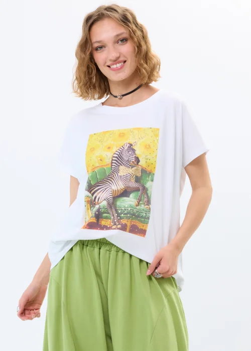 Biała bluzka oversize damska z kolorowym nadrukiem zebry na tle kwiatowego motywu. Luźny fason zestawiony z zielonymi spodniami tworzy nowoczesną, casualową stylizację.