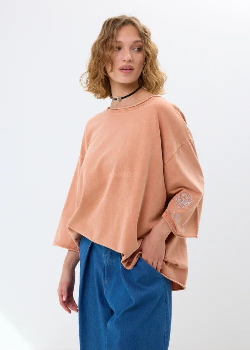 Oversize’owa bluzka w morelowym odcieniu z szerokimi rękawami i haftowanym kwiatem. Swobodny fason zapewnia wygodę i casualowy styl.