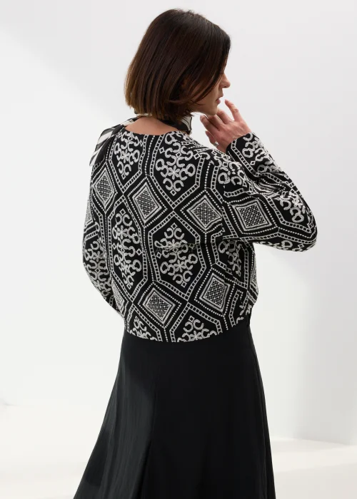 Czarno-biała koszula damska z efektownym haftowanym wzorem inspirowanym stylem boho i etnicznymi ornamentami. Luźny fason z szerokimi rękawami oraz kontrastowe zdobienia nadają modelowi wyjątkowego charakteru.