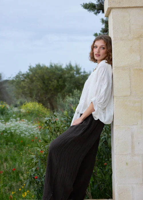 Biała koszula boho z haftowanymi kwiatami i ozdobnymi zapięciami w kształcie rozgwiazd. Zwiewny fason wiązany w talii, zestawiony z ciemną spódnicą maxi.