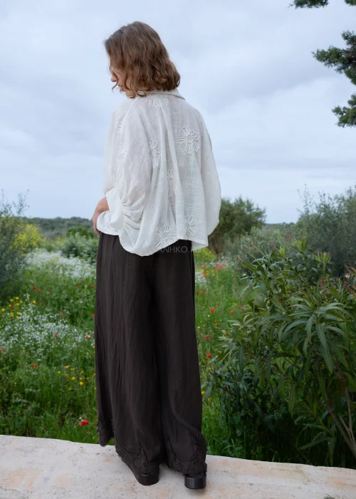 Biała koszula boho z haftowanymi kwiatami i ozdobnymi zapięciami w kształcie rozgwiazd. Zwiewny fason wiązany w talii, zestawiony z ciemną spódnicą maxi.