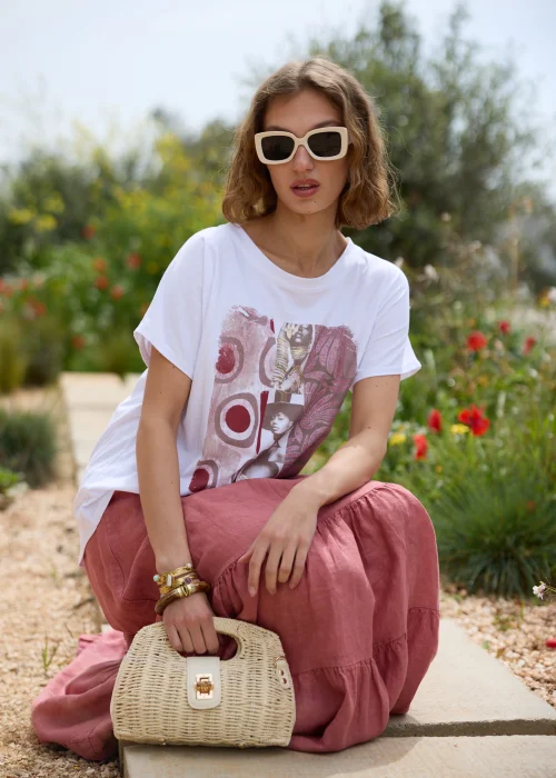 Biały T-shirt damski z artystycznym nadrukiem w odcieniach różu i bordo. Luźny fason z krótkim rękawem, zestawiony z lnianą spódnicą maxi w kolorze przygaszonego różu i naturalnymi dodatkami.