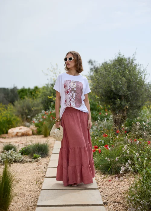 Biały T-shirt damski z artystycznym nadrukiem w odcieniach różu i bordo. Luźny fason z krótkim rękawem, zestawiony z lnianą spódnicą maxi w kolorze przygaszonego różu i naturalnymi dodatkami.