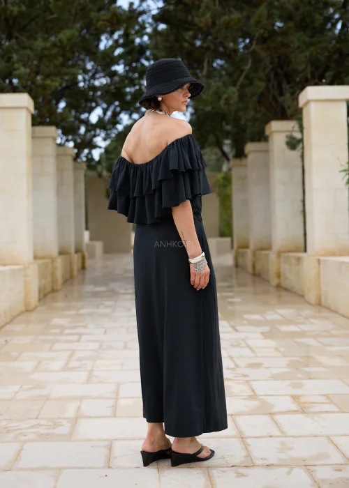 Czarna sukienka maxi hiszpanka z efektownymi falbanami przy dekolcie i regulacją w talii. Elegancka stylizacja z odkrytymi ramionami, kapeluszem i wyrazistą biżuterią w minimalistycznym wydaniu.