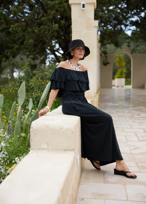 Czarna sukienka maxi hiszpanka z efektownymi falbanami przy dekolcie i regulacją w talii. Elegancka stylizacja z odkrytymi ramionami, kapeluszem i wyrazistą biżuterią w minimalistycznym wydaniu.