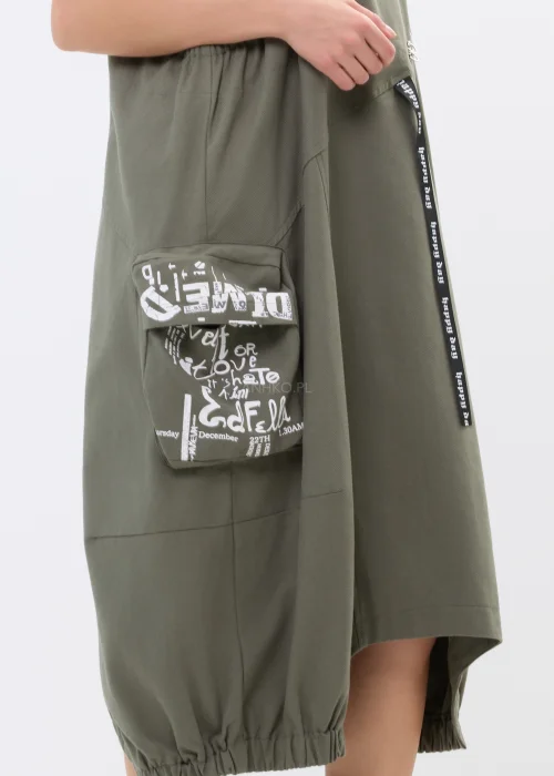 Khaki sukienka ogrodniczka z nadrukami, dużymi kieszeniami i regulowanymi szelkami. Luźny model w miejskim stylu z nowoczesnymi detalami i asymetrycznym fasonem.