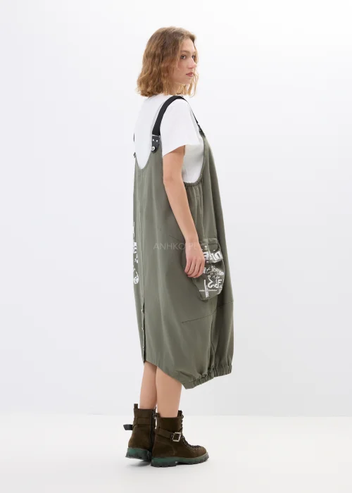 Khaki sukienka ogrodniczka z nadrukami, dużymi kieszeniami i regulowanymi szelkami. Luźny model w miejskim stylu z nowoczesnymi detalami i asymetrycznym fasonem.