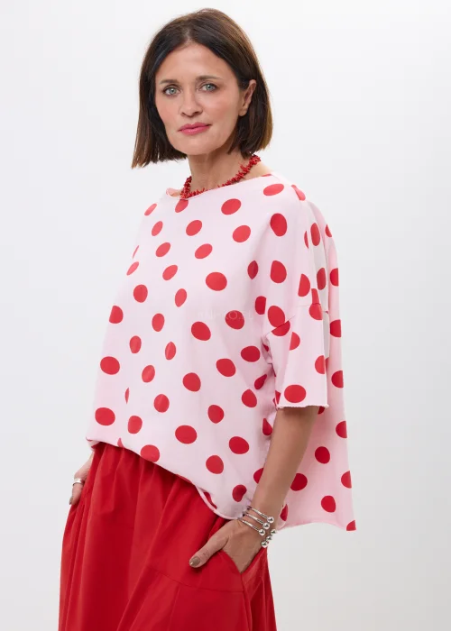 Różowa bluzka oversize w czerwone grochy z szerokim rękawem i minimalistycznym dekoltem. Kobiecy model idealny do  stylizacji w klimacie retro chic i casual fashion.