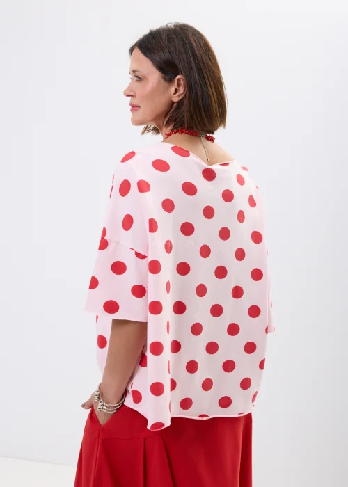 Różowa bluzka oversize w czerwone grochy z szerokim rękawem i minimalistycznym dekoltem. Kobiecy model idealny do  stylizacji w klimacie retro chic i casual fashion.