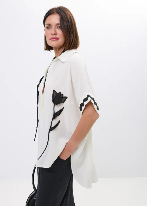 Koszula oversize ecru z kołnierzykiem i czarnymi aplikacjami kwiatowymi. Asymetryczny fason oraz kontrastowe detale nadają stylizacji elegancki, artystyczny charakter.