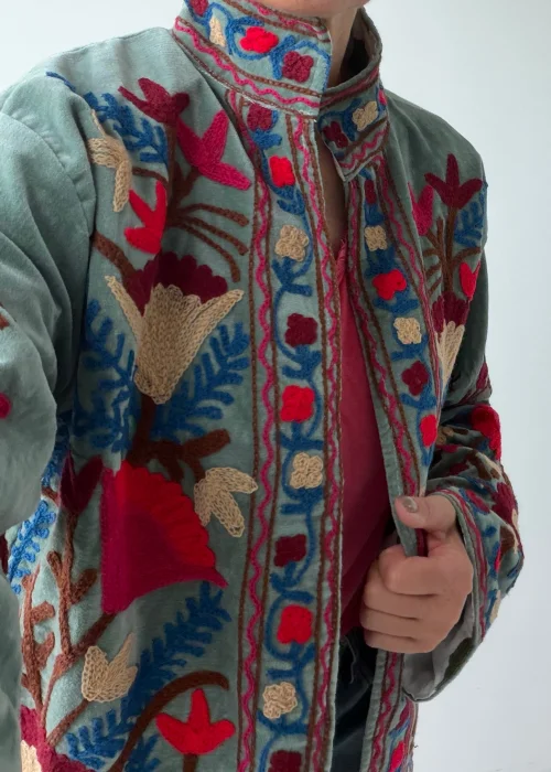 Żakiet damski w kolorze szałwiowej zieleni z bogatym haftem kwiatowym w odcieniach różu, beżu, błękitu i bordo. Artystyczny model w stylu boho z efektownymi roślinnymi zdobieniami.