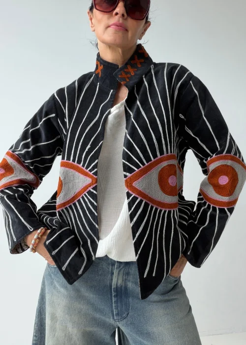 Żakiet damski w kolorze czarnym z efektownym haftem oka oraz promienistymi liniami w kontrastowym jasnym kolorze. Oryginalny model o artystycznym charakterze inspirowany symboliką „evil eye”.