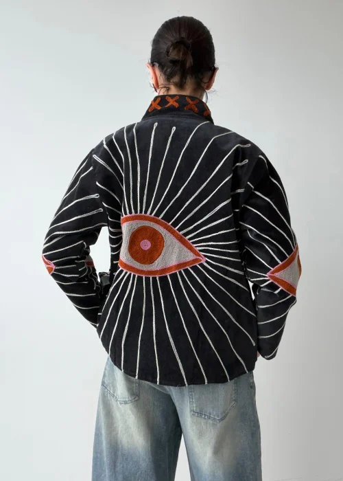 Żakiet damski w kolorze czarnym z efektownym haftem oka oraz promienistymi liniami w kontrastowym jasnym kolorze. Oryginalny model o artystycznym charakterze inspirowany symboliką „evil eye”.