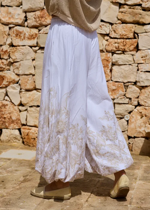 Białe szerokie spodnie z delikatnym roślinnym printem przy nogawkach. Lekki materiał i swobodny fason nadają modelowi kobiecego oraz artystycznego charakteru.