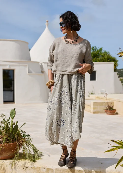 Sukienka w kolorze taupe z ozdobnym wzorem paisley w odcieniach beżu i błękitu. Zwiewny model o luźnym kroju z lnianą górą i rozkloszowanym dołem prezentowany w naturalnej stylizacji.