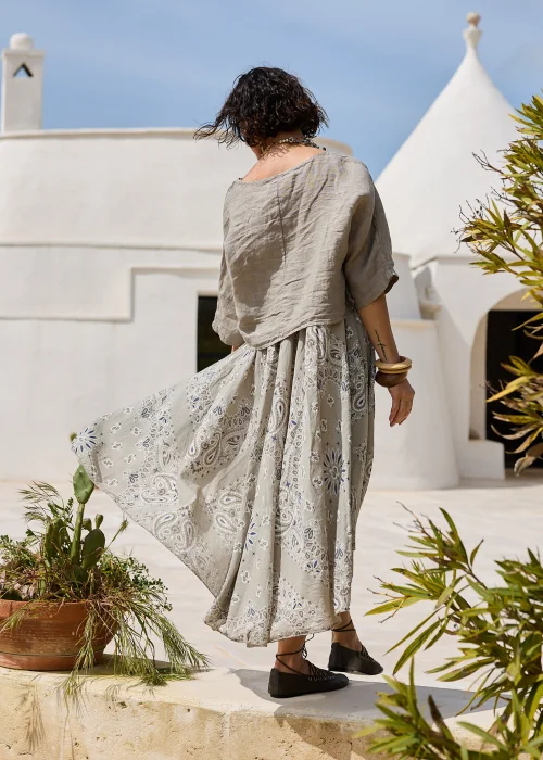 Sukienka w kolorze taupe z ozdobnym wzorem paisley w odcieniach beżu i błękitu. Zwiewny model o luźnym kroju z lnianą górą i rozkloszowanym dołem prezentowany w naturalnej stylizacji.