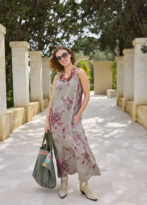 Lniana sukienka maxi w kolorze taupe z kwiatowym nadrukiem w odcieniach różu. Lekki model na szerokich ramiączkach o luźnym kroju, prezentowany w naturalnej stylizacji z kowbojkami i dużą torbą.