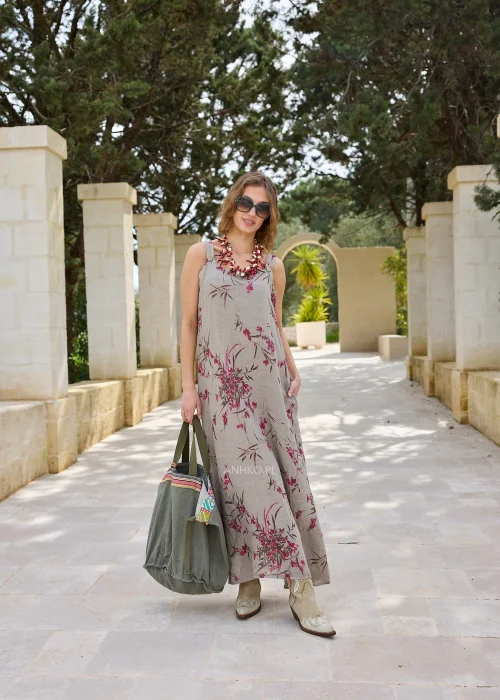 Lniana sukienka maxi w kolorze taupe z kwiatowym nadrukiem w odcieniach różu. Lekki model na szerokich ramiączkach o luźnym kroju, prezentowany w naturalnej stylizacji z kowbojkami i dużą torbą.