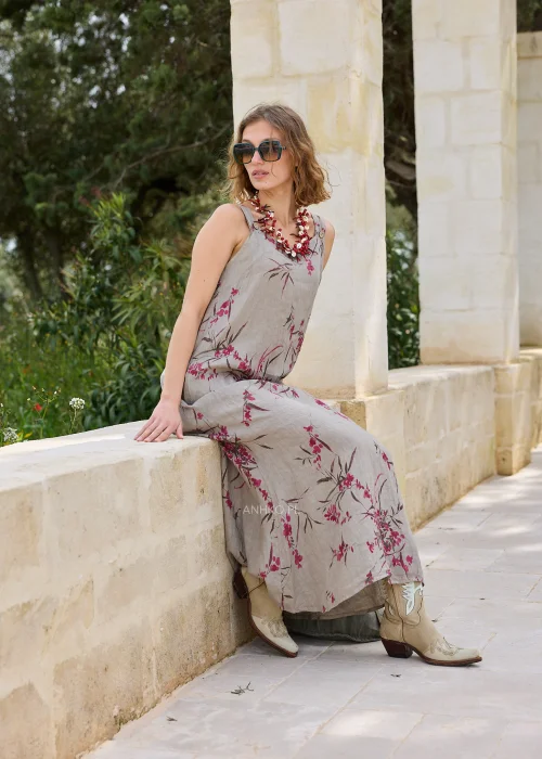 Lniana sukienka maxi w kolorze taupe z kwiatowym nadrukiem w odcieniach różu. Lekki model na szerokich ramiączkach o luźnym kroju, prezentowany w naturalnej stylizacji z kowbojkami i dużą torbą.