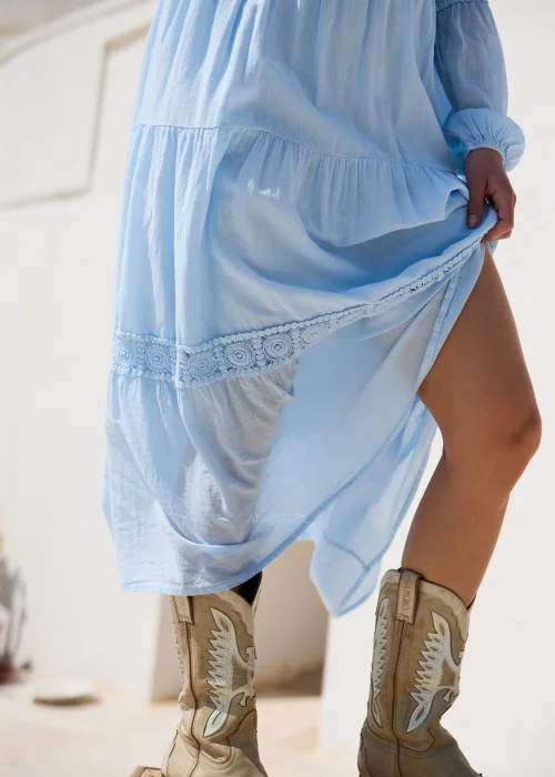 Błękitna sukienka boho maxi z koronkowymi wstawkami i długimi bufiastymi rękawami. Zwiewny fason z falbanami doskonale komponuje się z kowbojkami, tworząc romantyczną stylizację w stylu western chic.