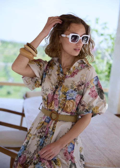 Sukienka maxi w kwiatowy wzór w stylu boho, z krótkimi bufiastymi rękawami i paskiem podkreślającym talię. Romantyczna stylizacja z kowbojkami i okularami przeciwsłonecznymi idealnie podkreśla artystyczny, rustykalny charakter modelu.