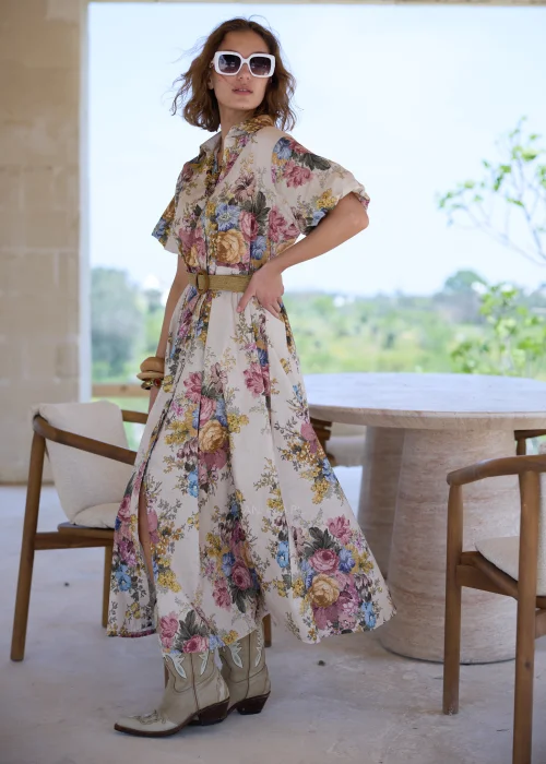 Sukienka maxi w kwiatowy wzór w stylu boho, z krótkimi bufiastymi rękawami i paskiem podkreślającym talię. Romantyczna stylizacja z kowbojkami i okularami przeciwsłonecznymi idealnie podkreśla artystyczny, rustykalny charakter modelu.