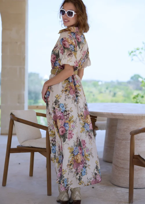 Sukienka maxi w kwiatowy wzór w stylu boho, z krótkimi bufiastymi rękawami i paskiem podkreślającym talię. Romantyczna stylizacja z kowbojkami i okularami przeciwsłonecznymi idealnie podkreśla artystyczny, rustykalny charakter modelu.