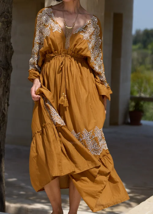 Karmelowa sukienka boho midi z ozdobną koronką i haftowanymi wstawkami przy dekolcie, rękawach oraz dole. Kobiecy fason z wiązaniem w talii i falbaną tworzy elegancką stylizację w klimacie śródziemnomorskim.