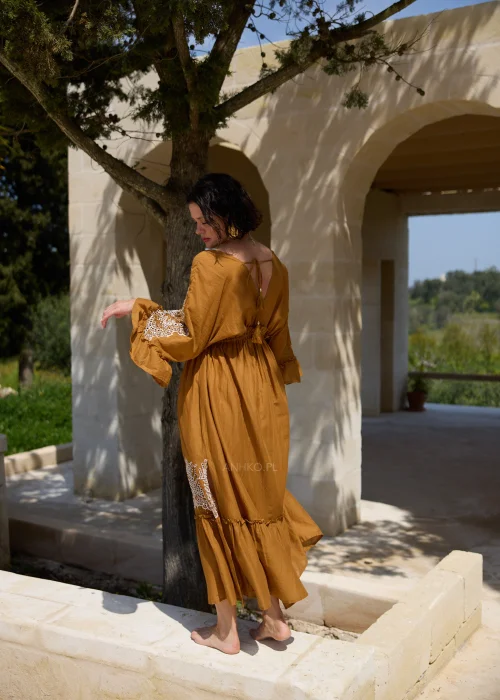 Karmelowa sukienka boho midi z ozdobną koronką i haftowanymi wstawkami przy dekolcie, rękawach oraz dole. Kobiecy fason z wiązaniem w talii i falbaną tworzy elegancką stylizację w klimacie śródziemnomorskim.