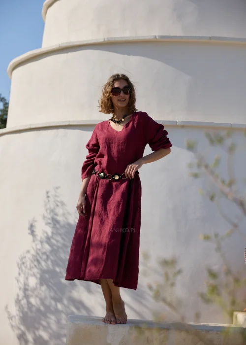 Bordowa lniana sukienka midi z dekoltem V i długimi rękawami o luźnym, naturalnym fasonie. Minimalistyczny krój podkreśla elegancję stylizacji w klimacie boho i slow fashion.