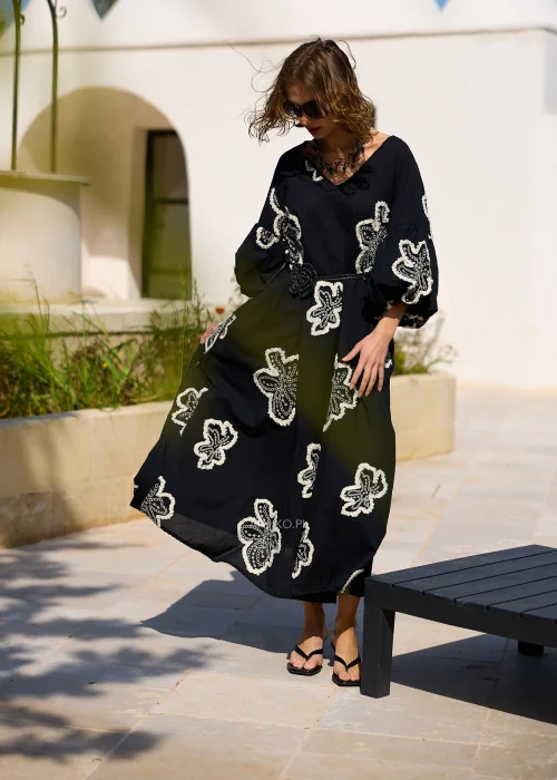 Czarna sukienka maxi z efektownymi białymi haftami w kształcie kwiatów, bufiastymi rękawami i ozdobnym paskiem w talii. Zwiewny model w stylu boho, idealny na eleganckie i codzienne stylizacje z kobiecym charakterem.