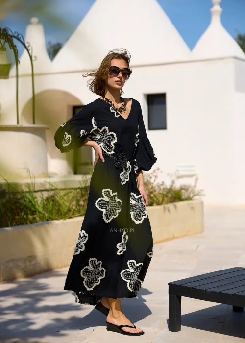 Czarna sukienka maxi z efektownymi białymi haftami w kształcie kwiatów, bufiastymi rękawami i ozdobnym paskiem w talii. Zwiewny model w stylu boho, idealny na eleganckie i codzienne stylizacje z kobiecym charakterem.