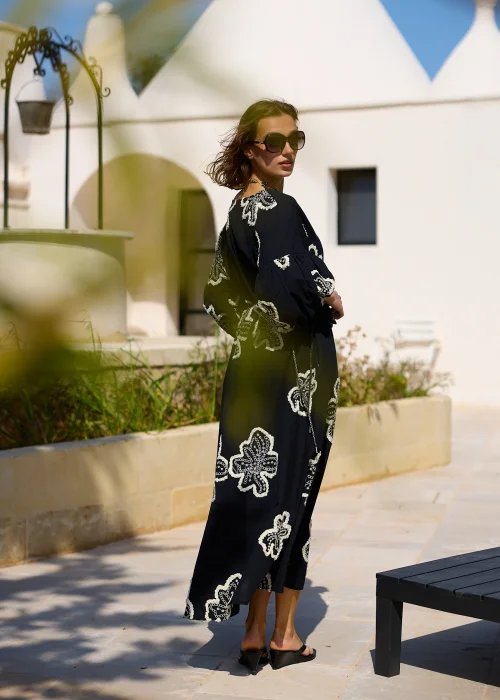 Czarna sukienka maxi z efektownymi białymi haftami w kształcie kwiatów, bufiastymi rękawami i ozdobnym paskiem w talii. Zwiewny model w stylu boho, idealny na eleganckie i codzienne stylizacje z kobiecym charakterem.