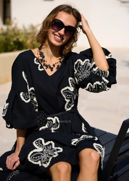 Czarna sukienka maxi z efektownymi białymi haftami w kształcie kwiatów, bufiastymi rękawami i ozdobnym paskiem w talii. Zwiewny model w stylu boho, idealny na eleganckie i codzienne stylizacje z kobiecym charakterem.